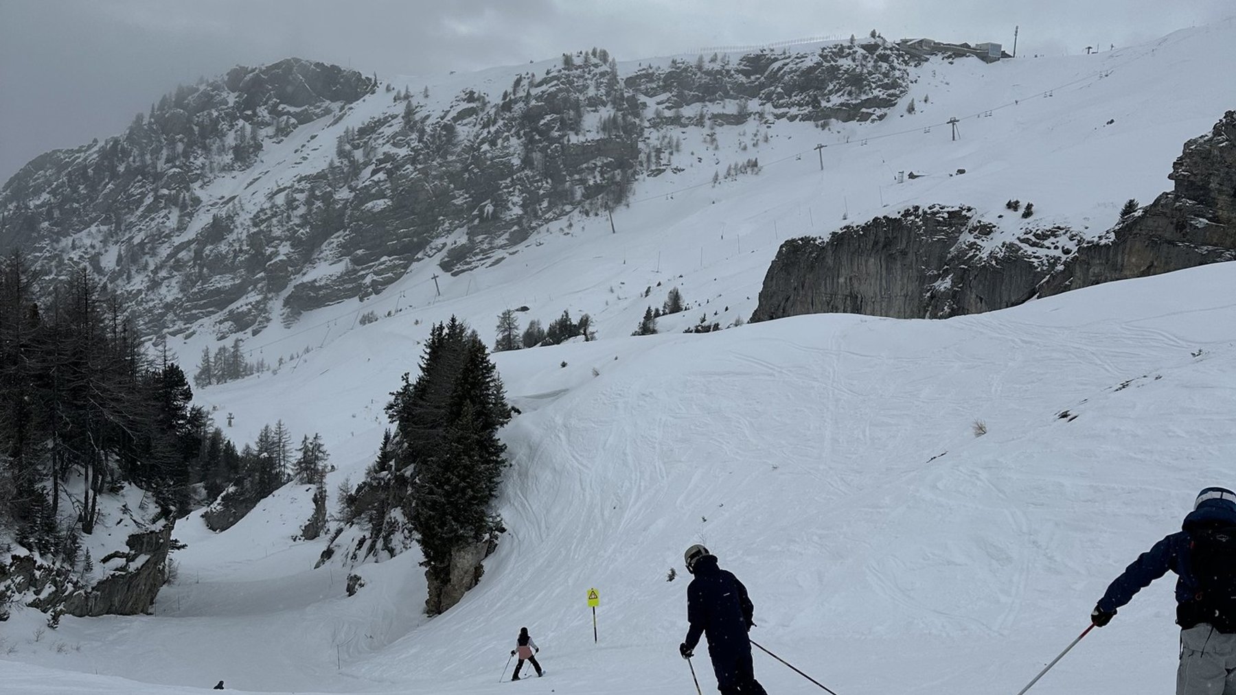 Skiers descending snowy alpine slopes under cloudy skies in a mountain ski resort