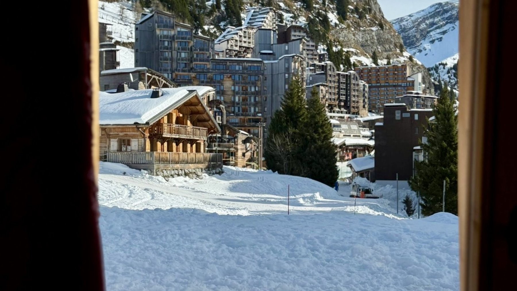 Snowy alpine village viewed through a window, with ski slopes and mountains in the distance