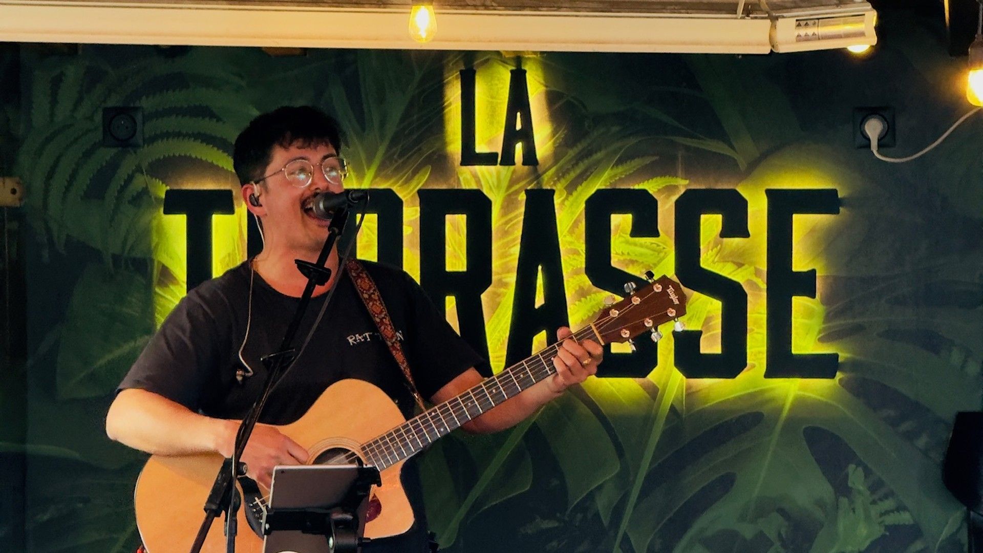 Musician singing and playing acoustic guitar during a live performance at La Terrasse.