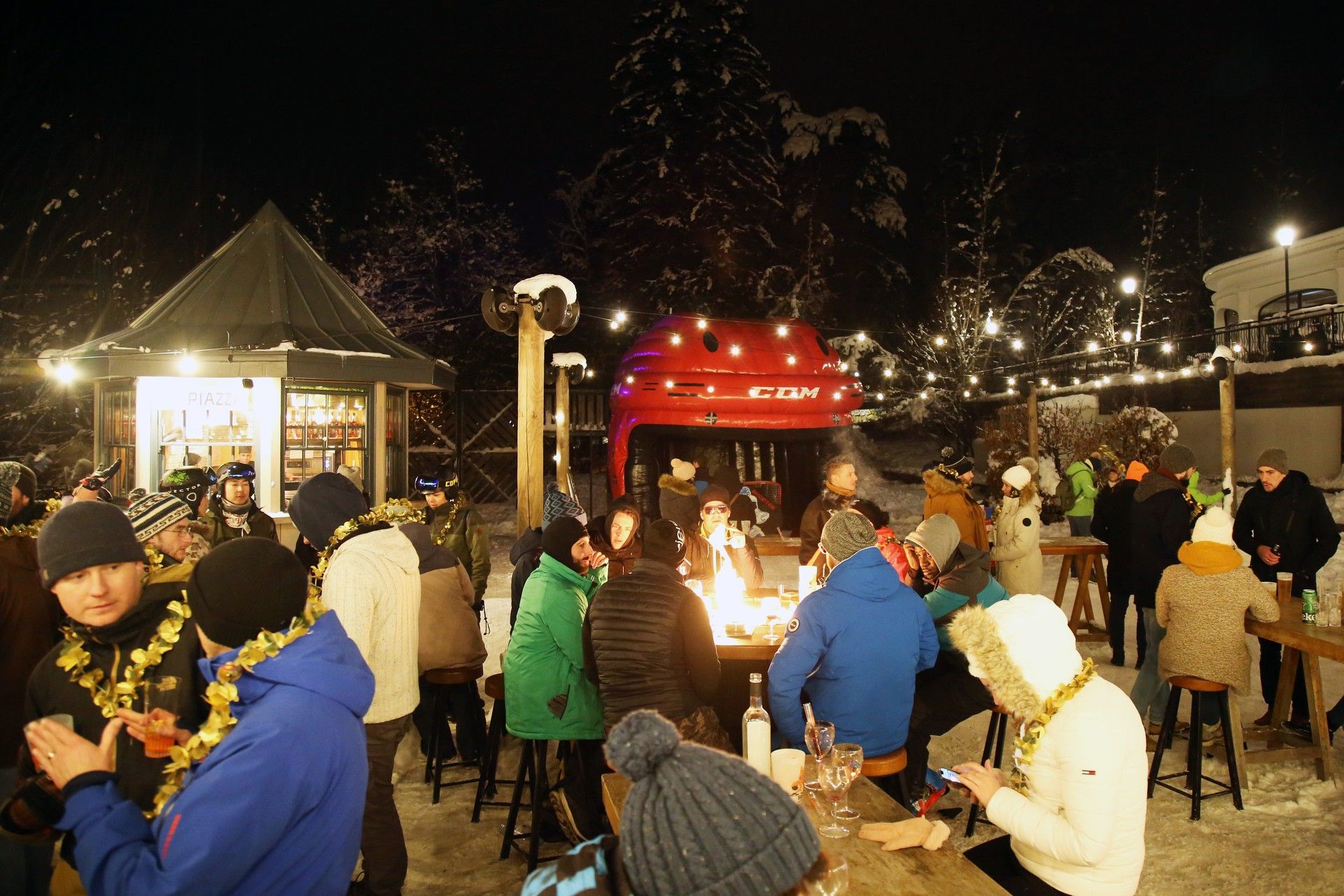 Night-time ski resort social scene with people mingling around outdoor food stalls and warm lights