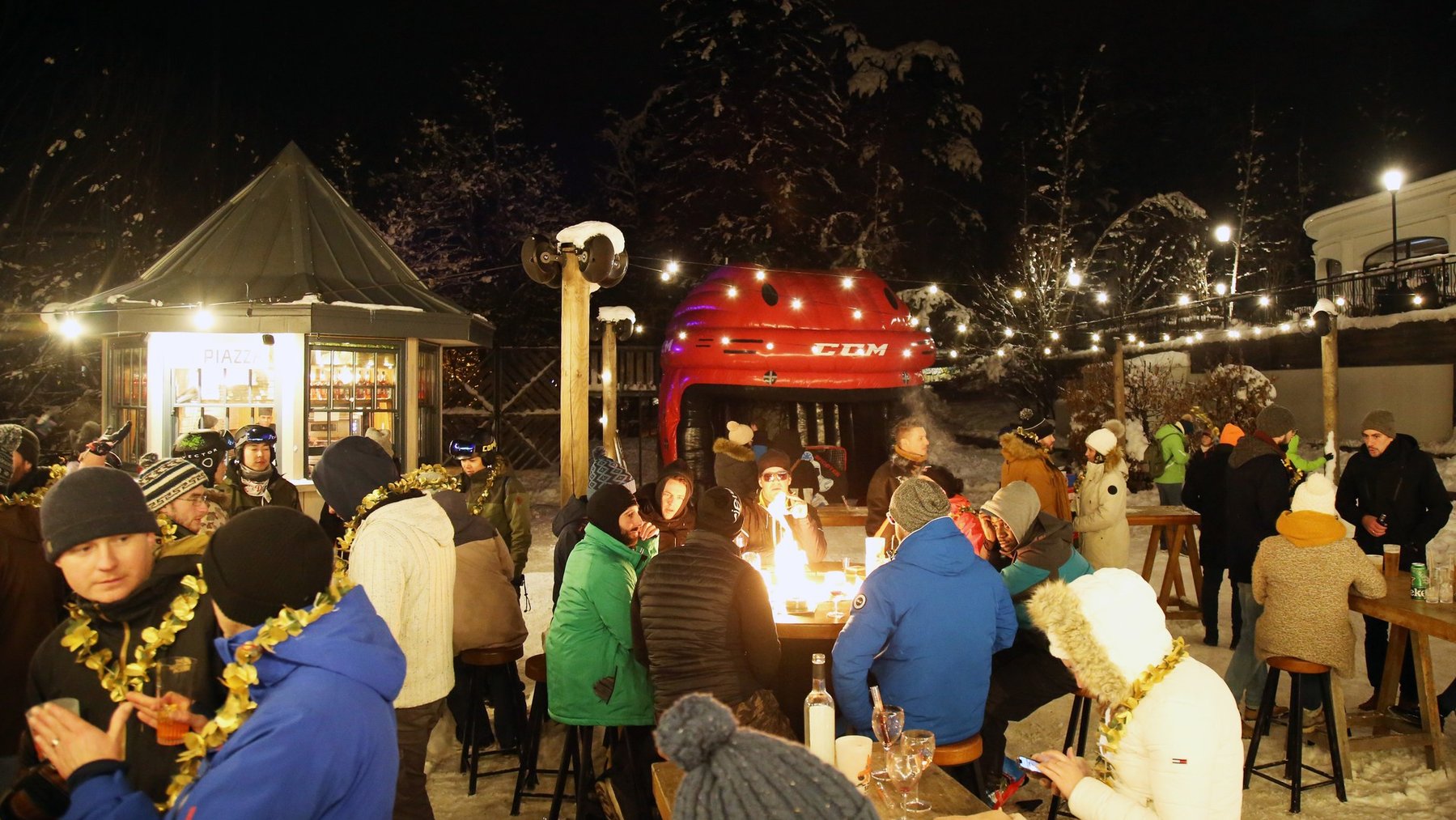 Night-time ski resort social scene with people mingling around outdoor food stalls and warm lights