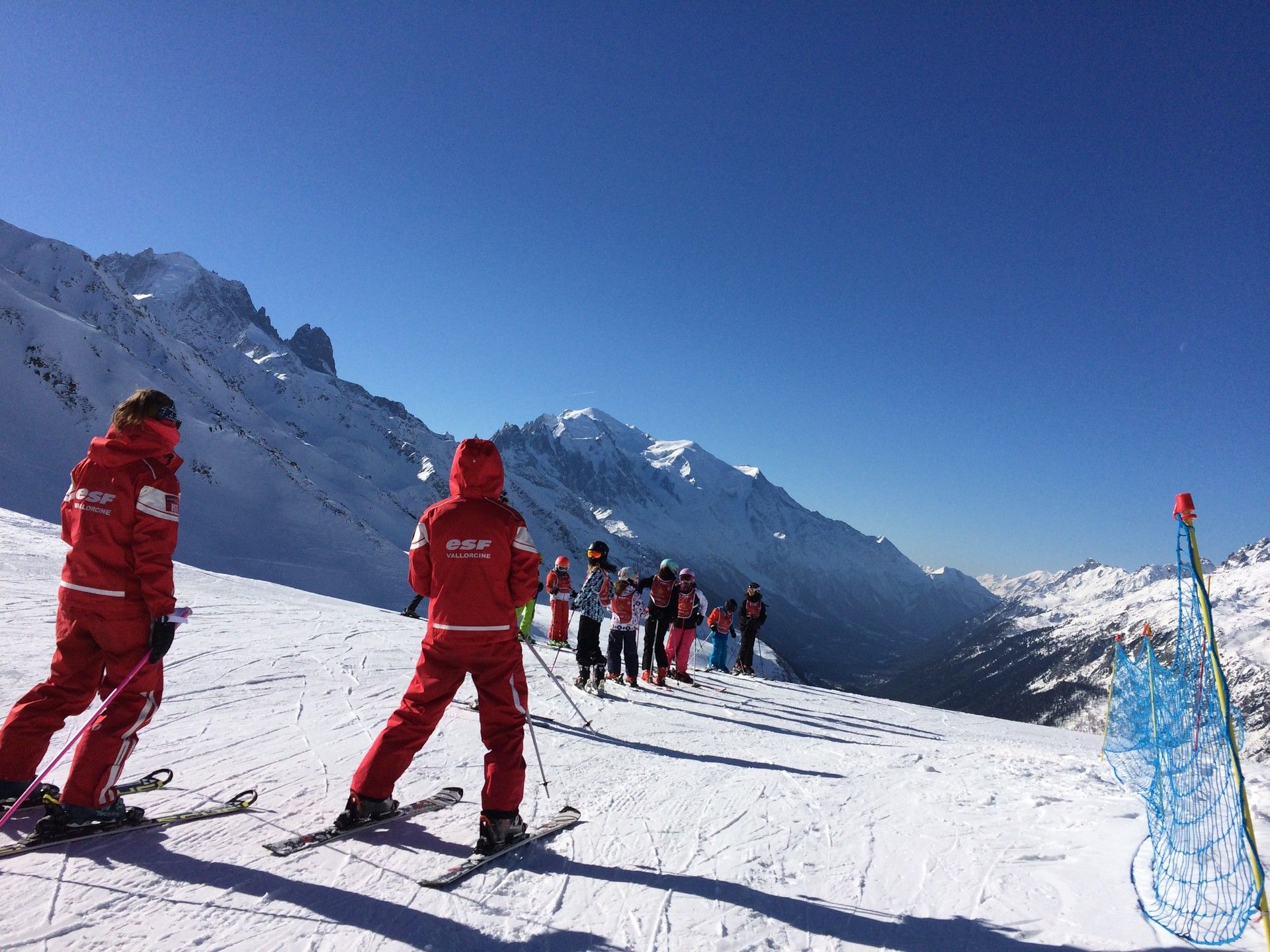 Ski patrol and group on a snowy mountain slope under clear blue skies