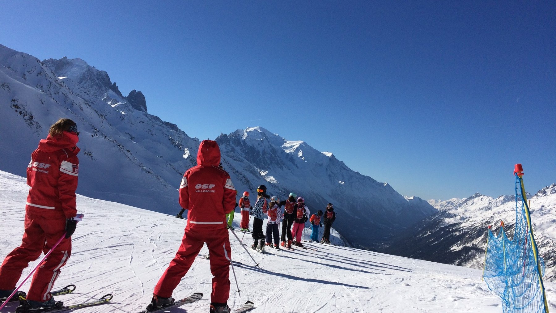 Ski patrol and group on a snowy mountain slope under clear blue skies