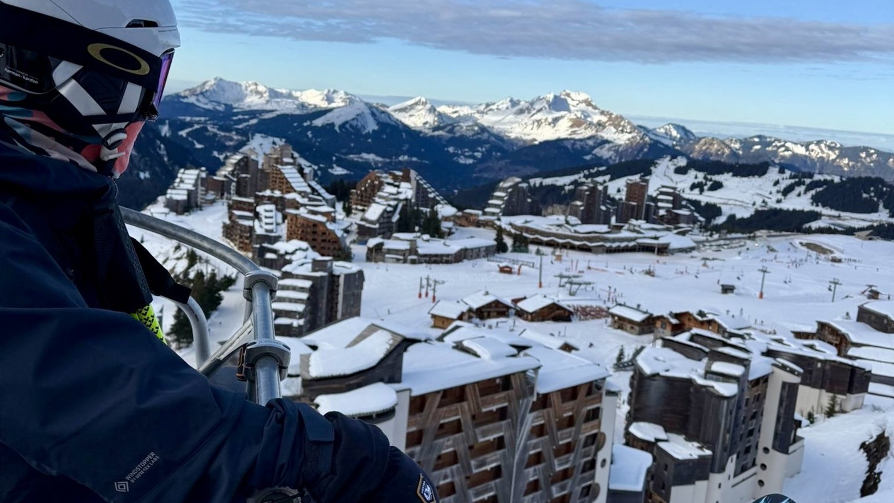 Skiing helmeted rider on chairlift with snowy mountain town and peaks in the background