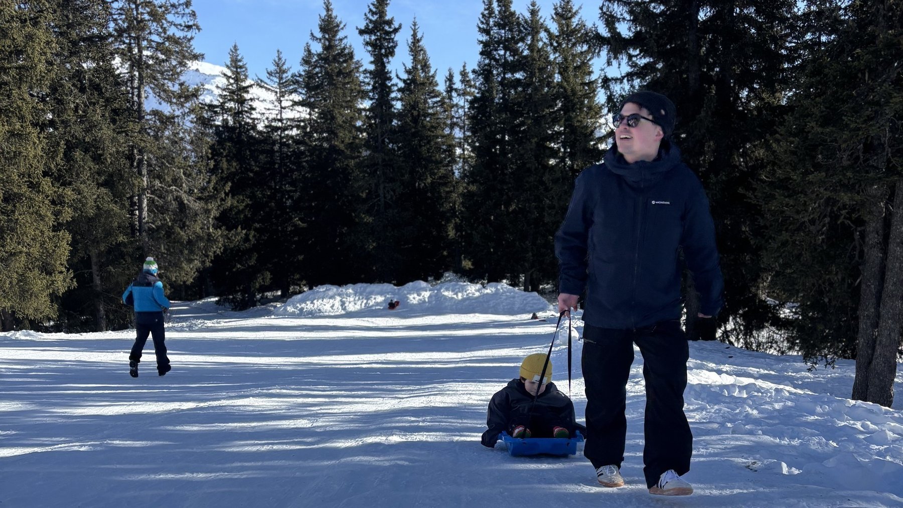 Skiing on a snowy forest path with a man walking and snow kicking in bright winter light