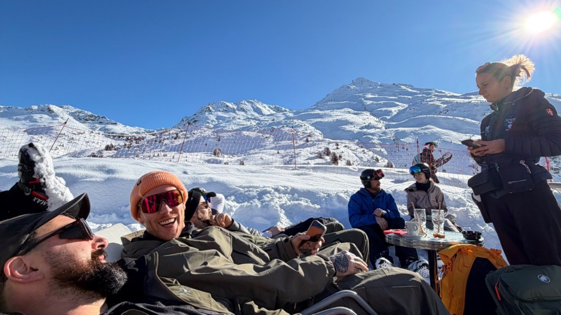 Skiers relax in the snow at Courchevel, with a mountain backdrop and a woman standing beside them.