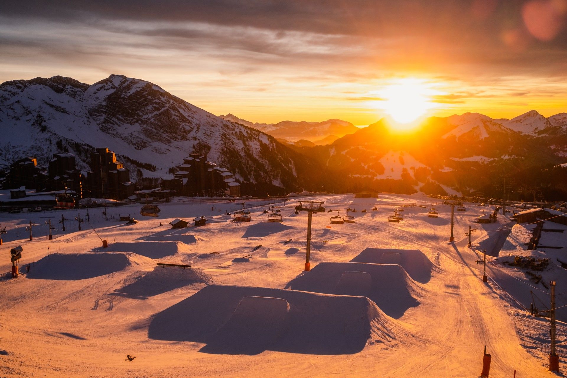 Snow-covered ski resort at sunset with dramatic alpine mountains and empty pistes