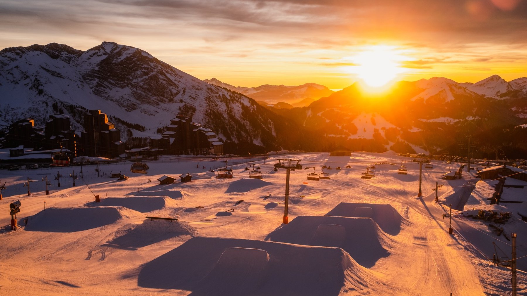 Snow-covered ski resort at sunset with dramatic alpine mountains and empty pistes