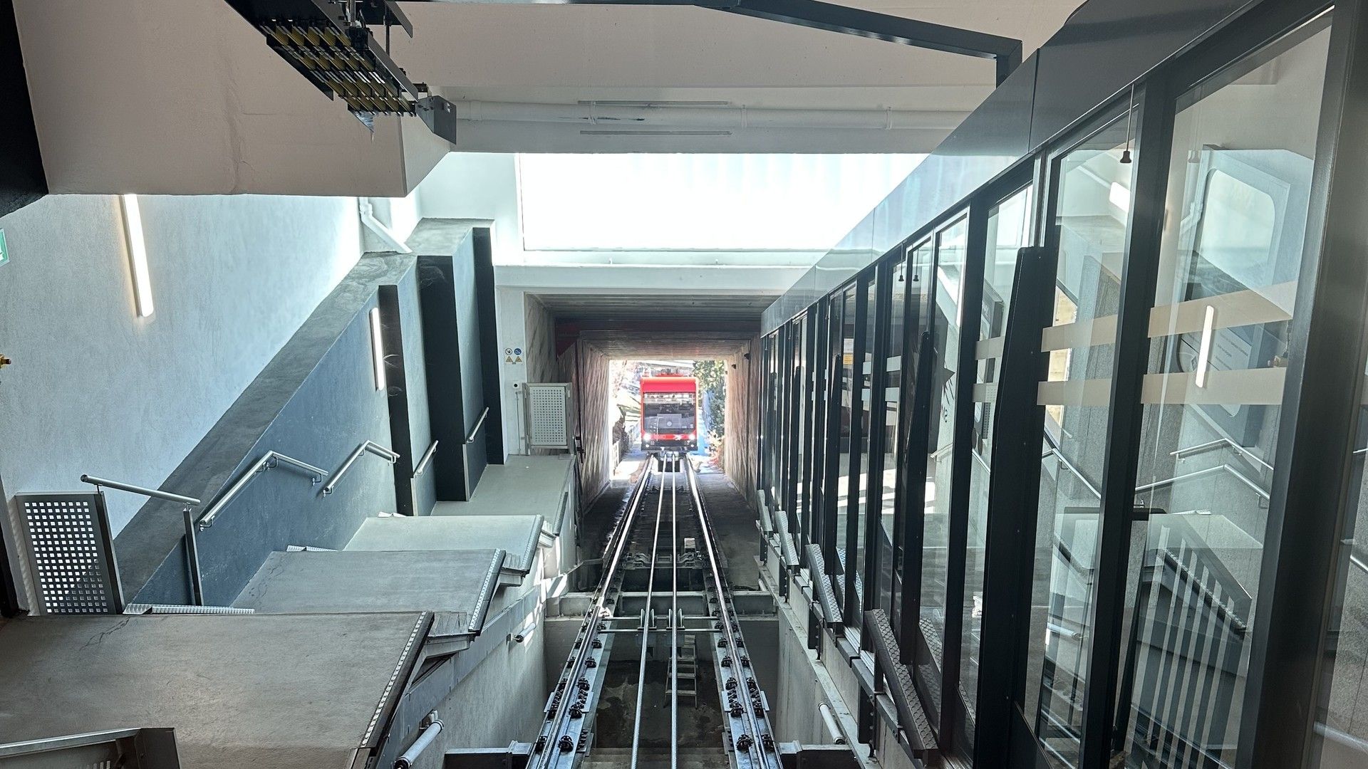 Indoor view down a long ski-run style track with barriers, benches, and glass railing