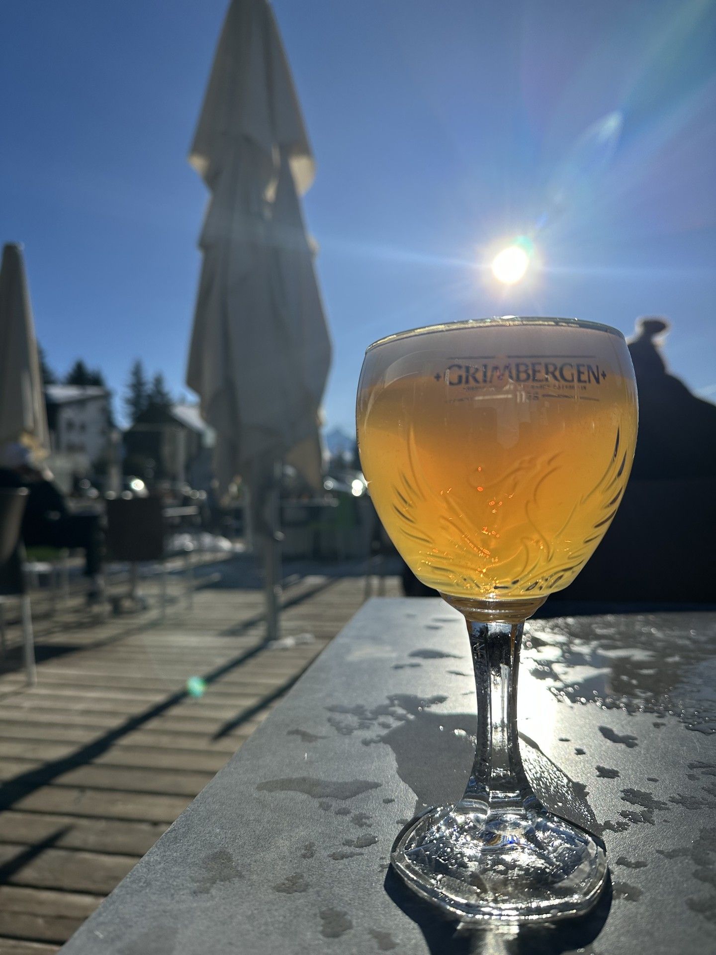 Golden beer in a glass on a lakeside terrace at sunset, with bright sun flares behind an umbrella