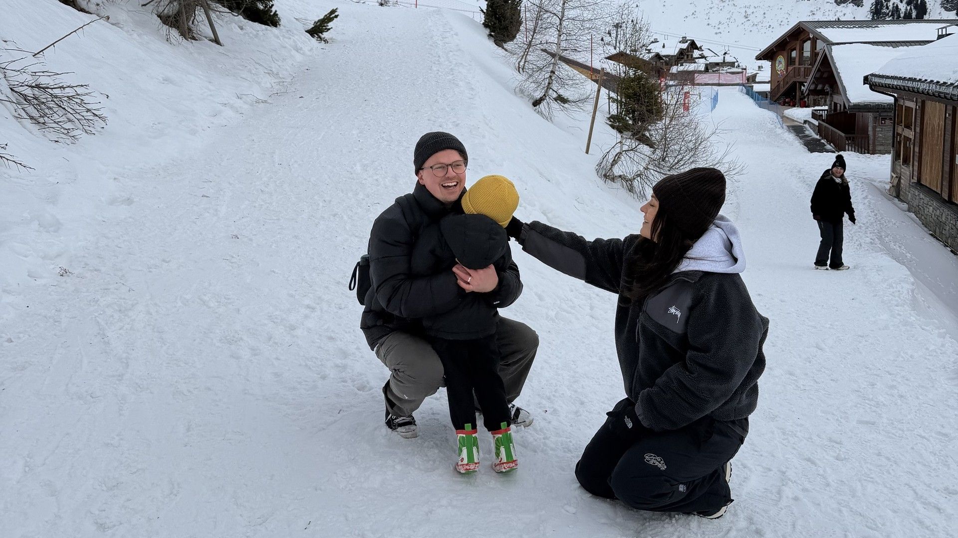 Two people chatting and smiling in the snow on a ski village path with mountains behind them