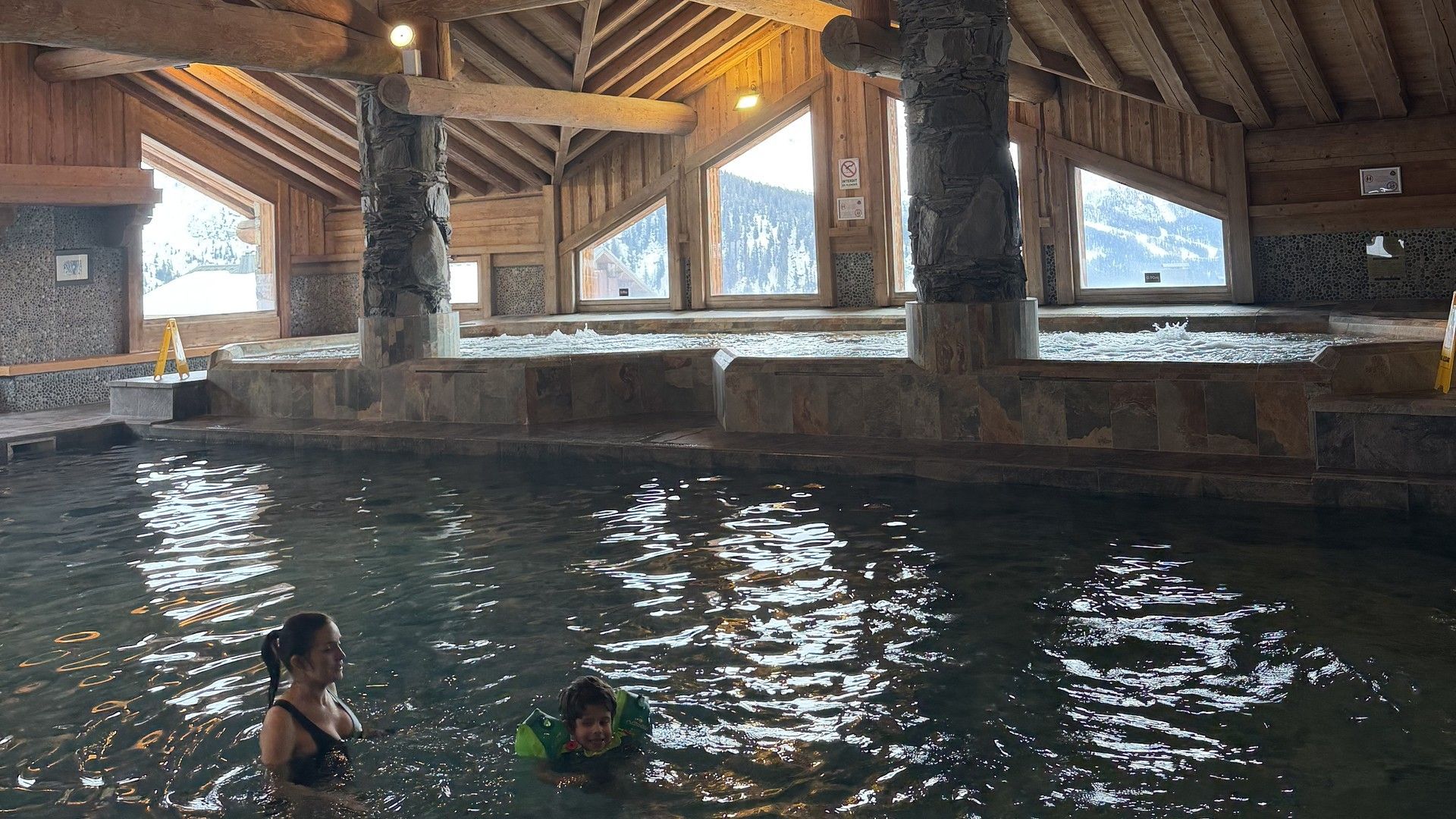 Indoor spa pool under wooden ceiling with visitors swimming and relaxing