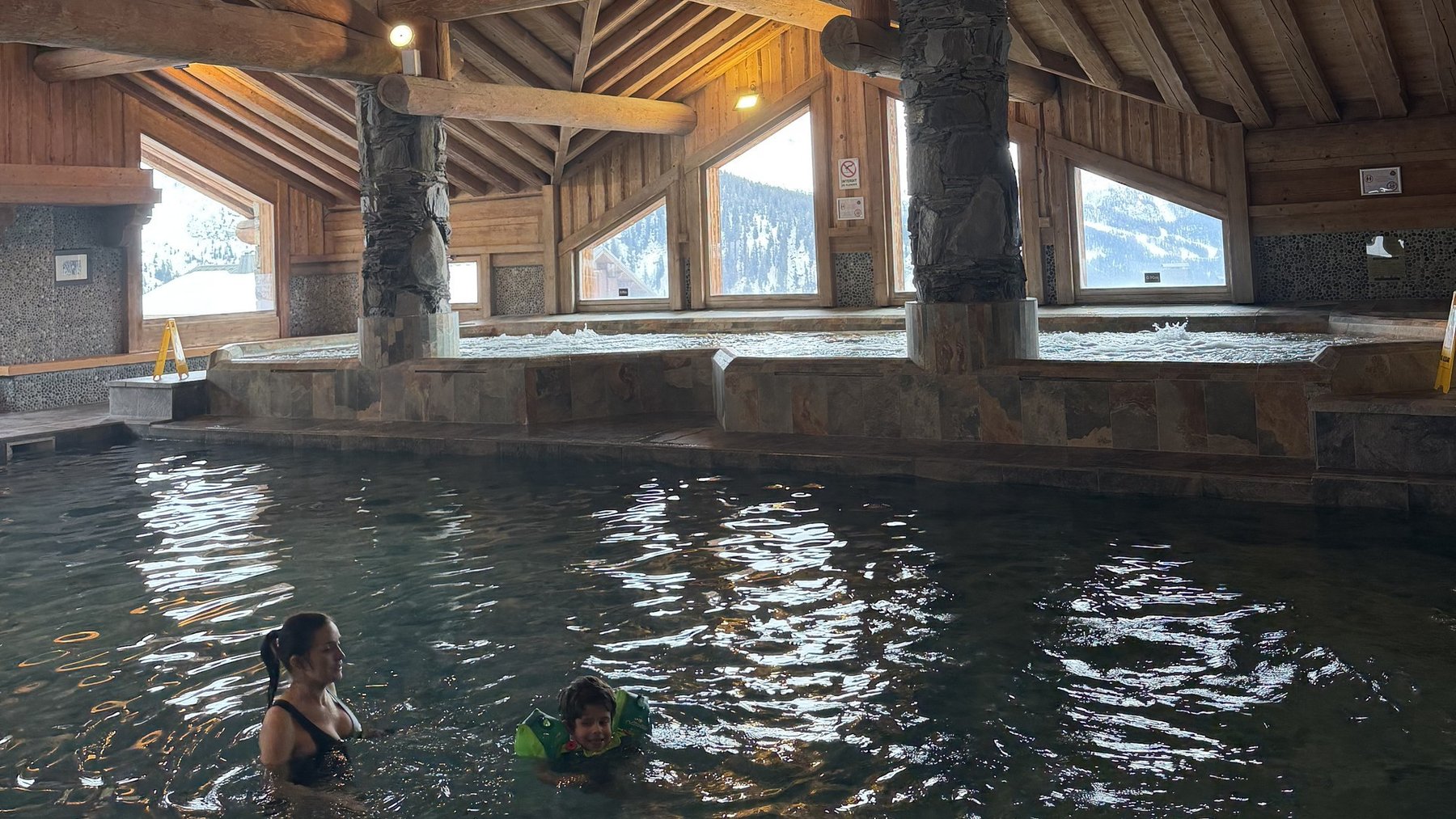 Indoor spa pool under wooden ceiling with visitors swimming and relaxing