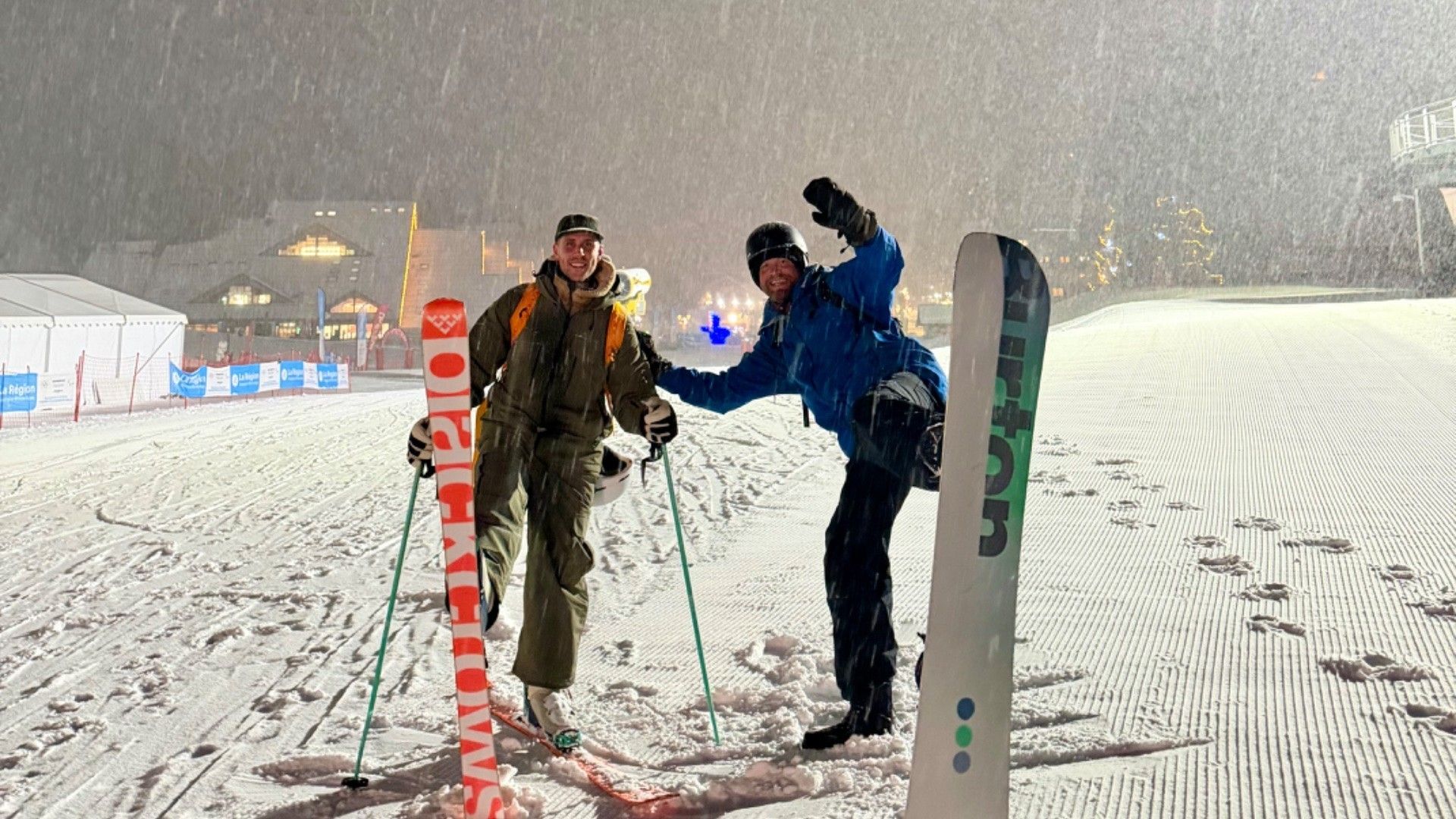 Two skiers descend a floodlit Méribel piste as heavy snow falls, one raising an arm