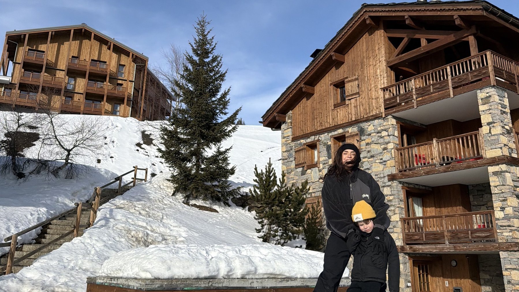 Person posing in deep snow in front of alpine chalets under a clear blue sky