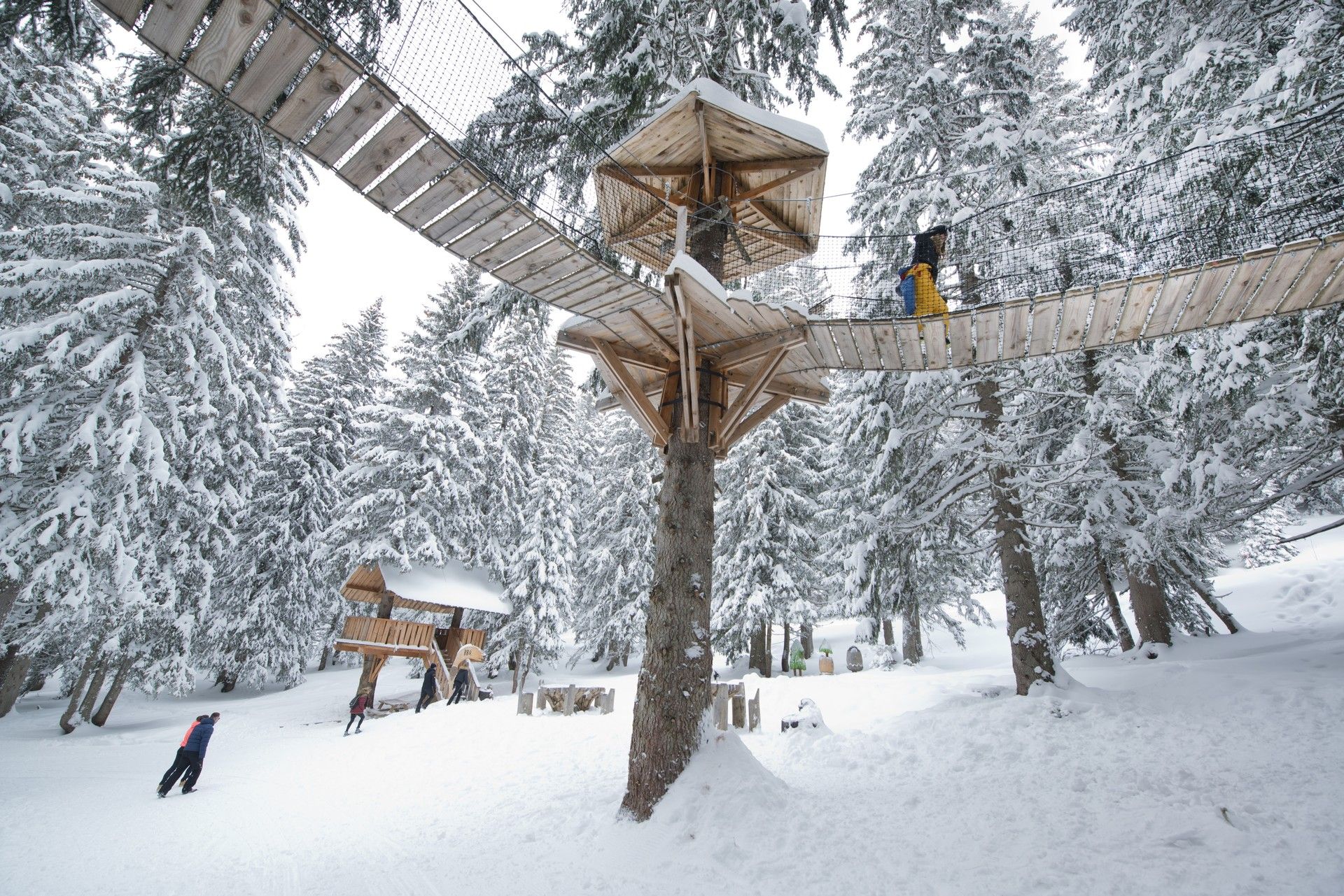 Snow-covered ski slope with wooden lift support and skier passing under winter installations