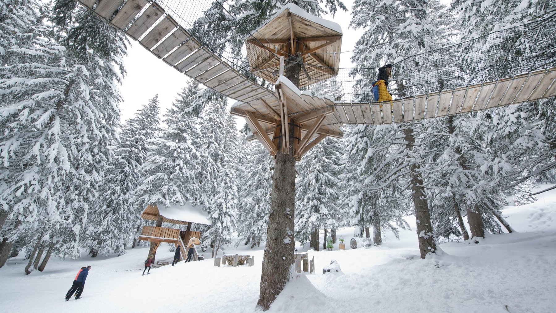 Snow-covered ski slope with wooden lift support and skier passing under winter installations