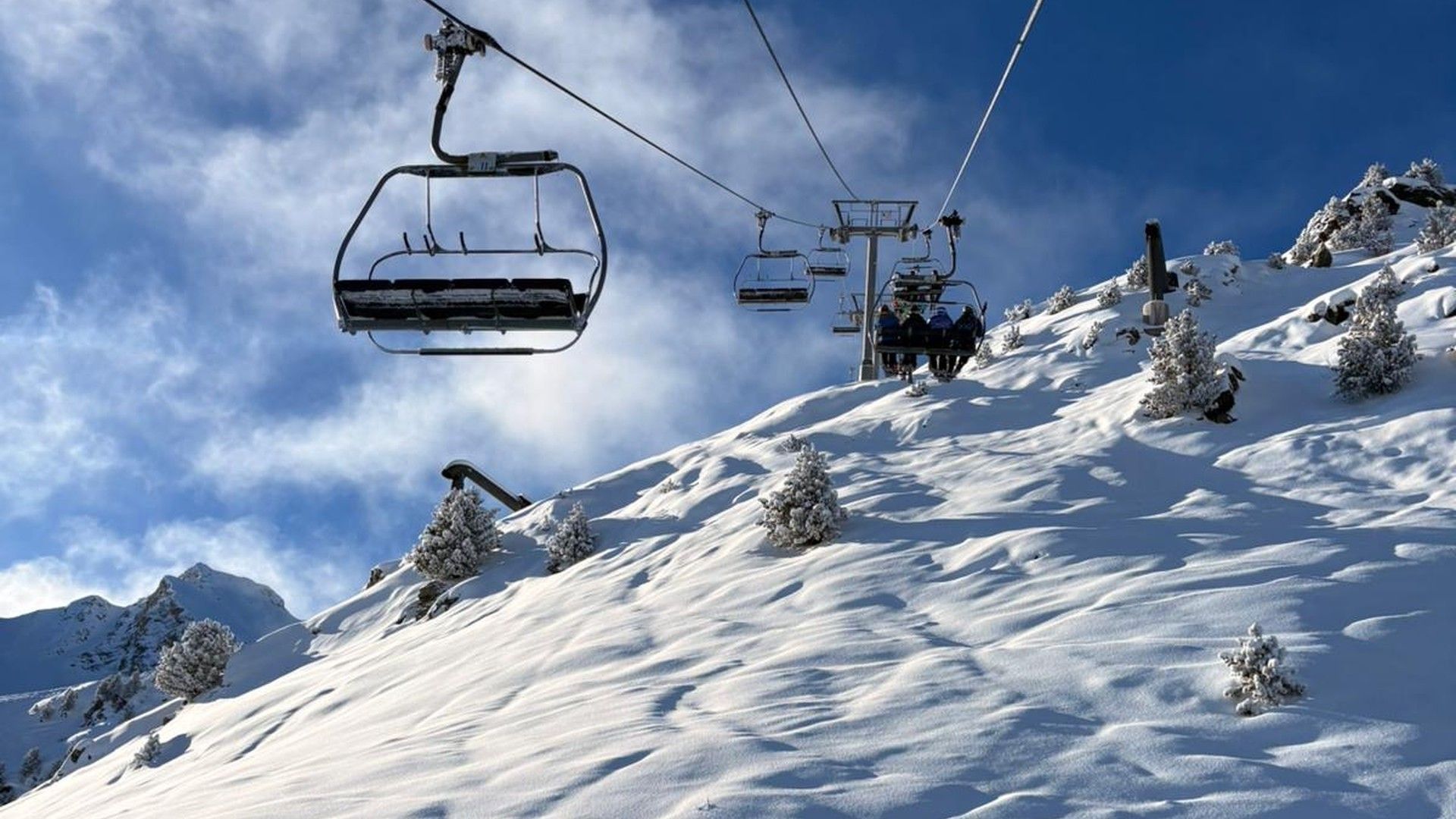 A chairlift rises above a snow-covered ski slope in Courchevel beneath a blue sky.