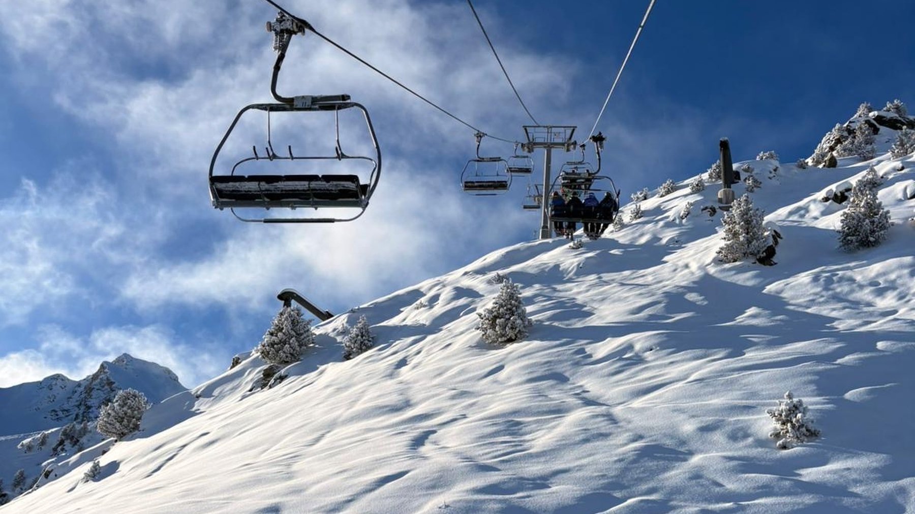 A chairlift rises above a snow-covered ski slope in Courchevel beneath a blue sky.