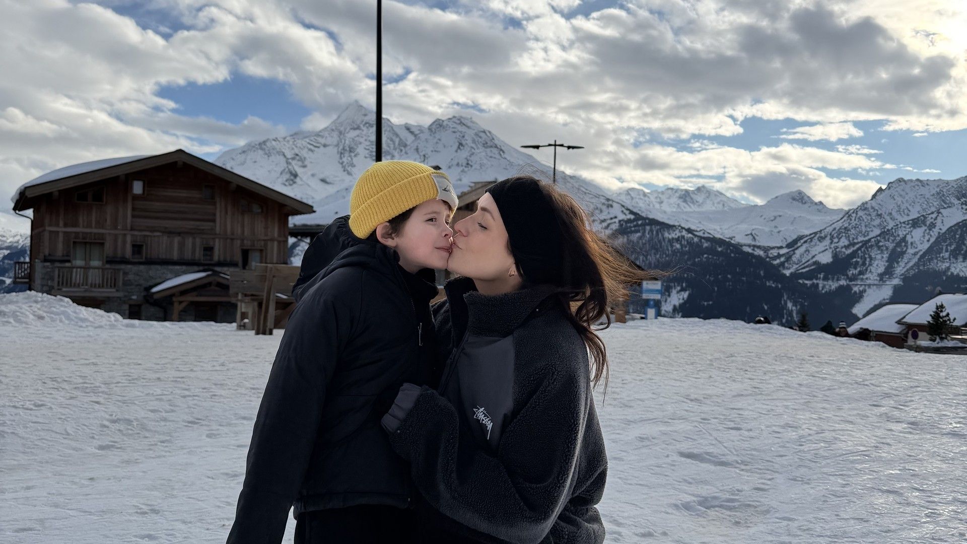 Couple in ski resort winter landscape kissing in snowy mountains under cloudy sky