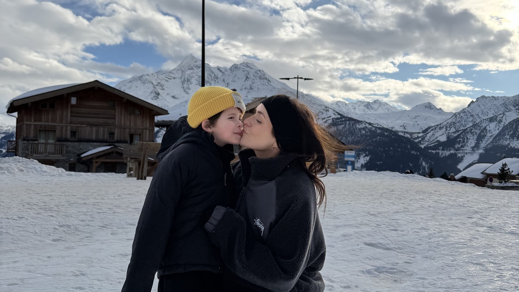 Couple in ski resort winter landscape kissing in snowy mountains under cloudy sky