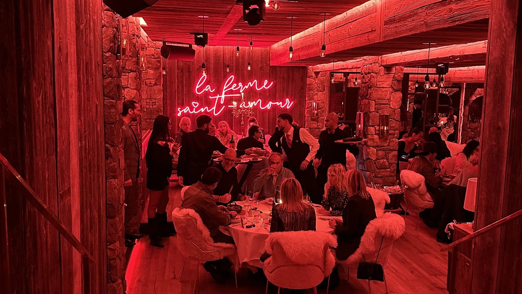 Red-lit dining room with guests seated at tables under a wooden ceiling and wall display