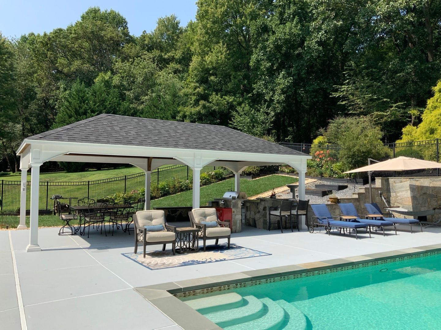 White pavilion beside a pool, over a patio with chairs and a dining table