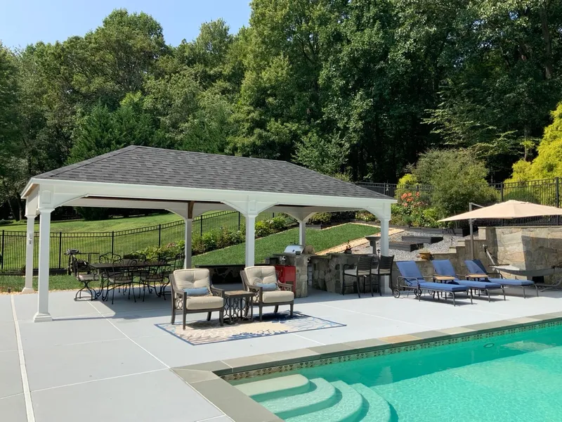 White pavilion beside a pool, over a patio with chairs and a dining table