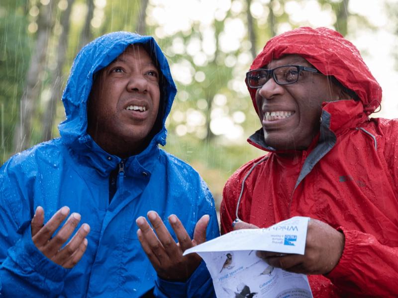 RSPB Big Garden Bird Watch campaign - Two men stood in woodland bird spotting while the rain is coming down each wearing a raincoat with one in red and the other in blue.