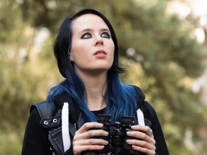 RSPB Big Garden Bird Watch campaign - A Goth girl stood in open woodland holding binoculars while looking towards the sky.