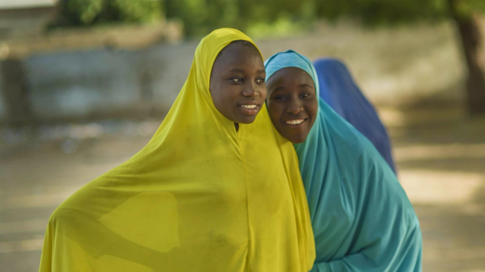Mines Advisory Group two smiling African girls wrapped in yellow and blue coverings