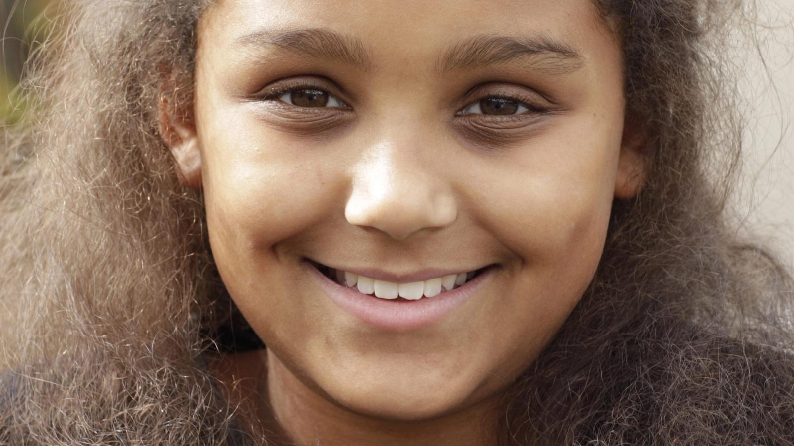 Close up of a teenage girl with brown curly hair smiling profusely at the camera
