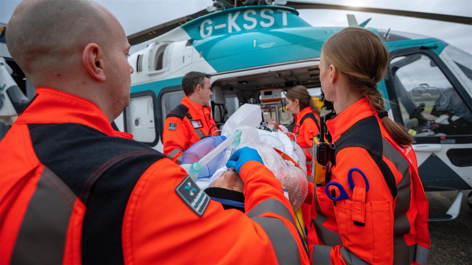 Paramedics in high vis clothing surrounding a patient on a gurney being placed into a KSS helicopter