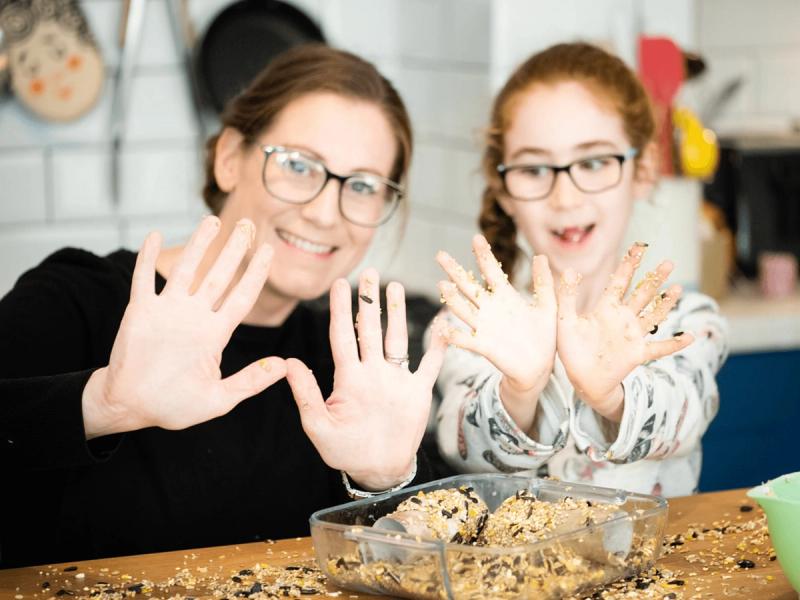 RSPB Big Garden Bird Watch campaign - A mother and daughter in their kitchen making seed cakes for birds with both of them showing mixture covered hands to the camera.