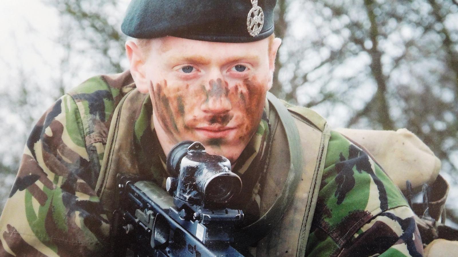 Royal Star & Garter - A relative close up of a young army veteran, Stephen, in fatigues holding a rifle while prone looking across the camera lens.