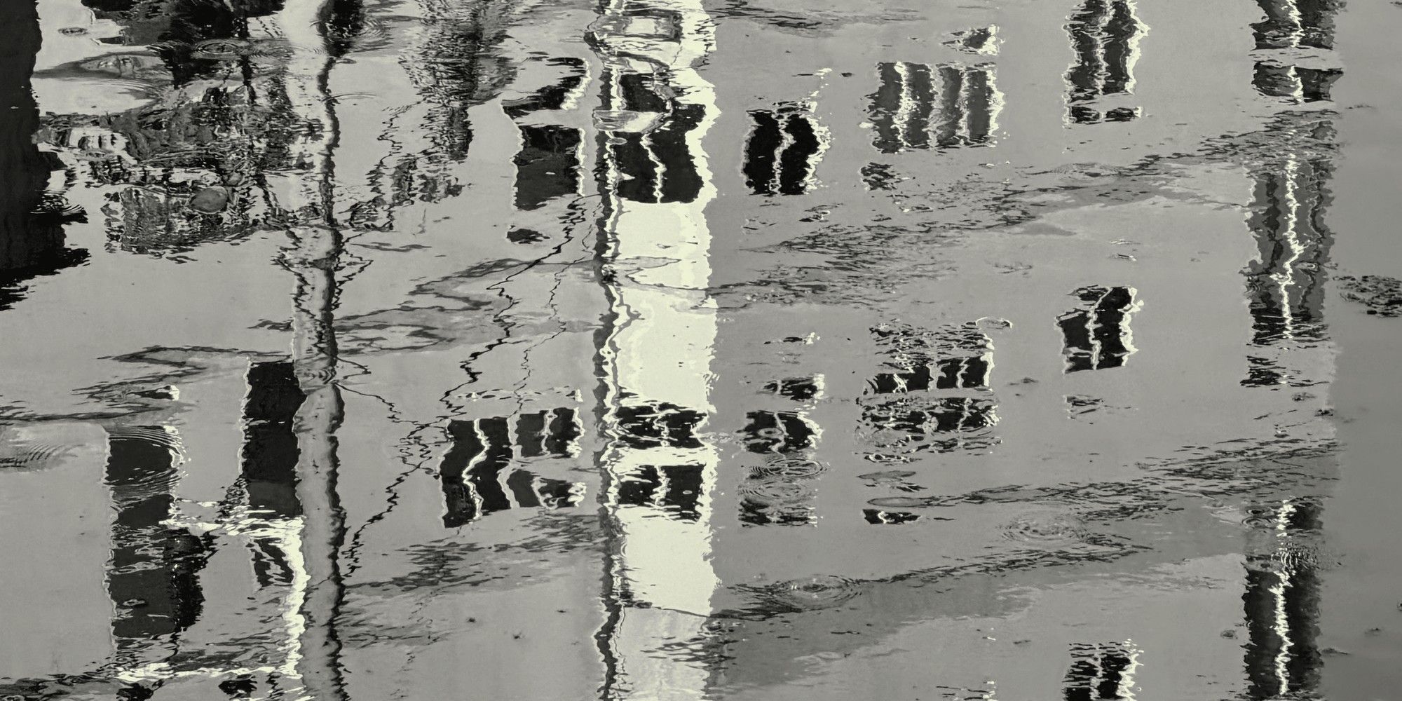 Black-and-white rippling water reflecting distorted tall buildings, standing for the unclear picture that emerges before scaling AI.