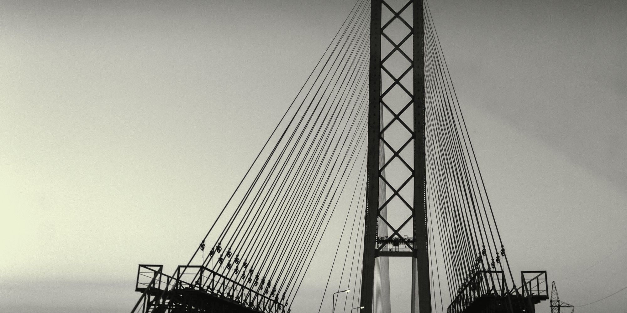 A tall latticed suspension bridge tower with fanned steel cables descending to the roadway, standing for the value of long-term connections.