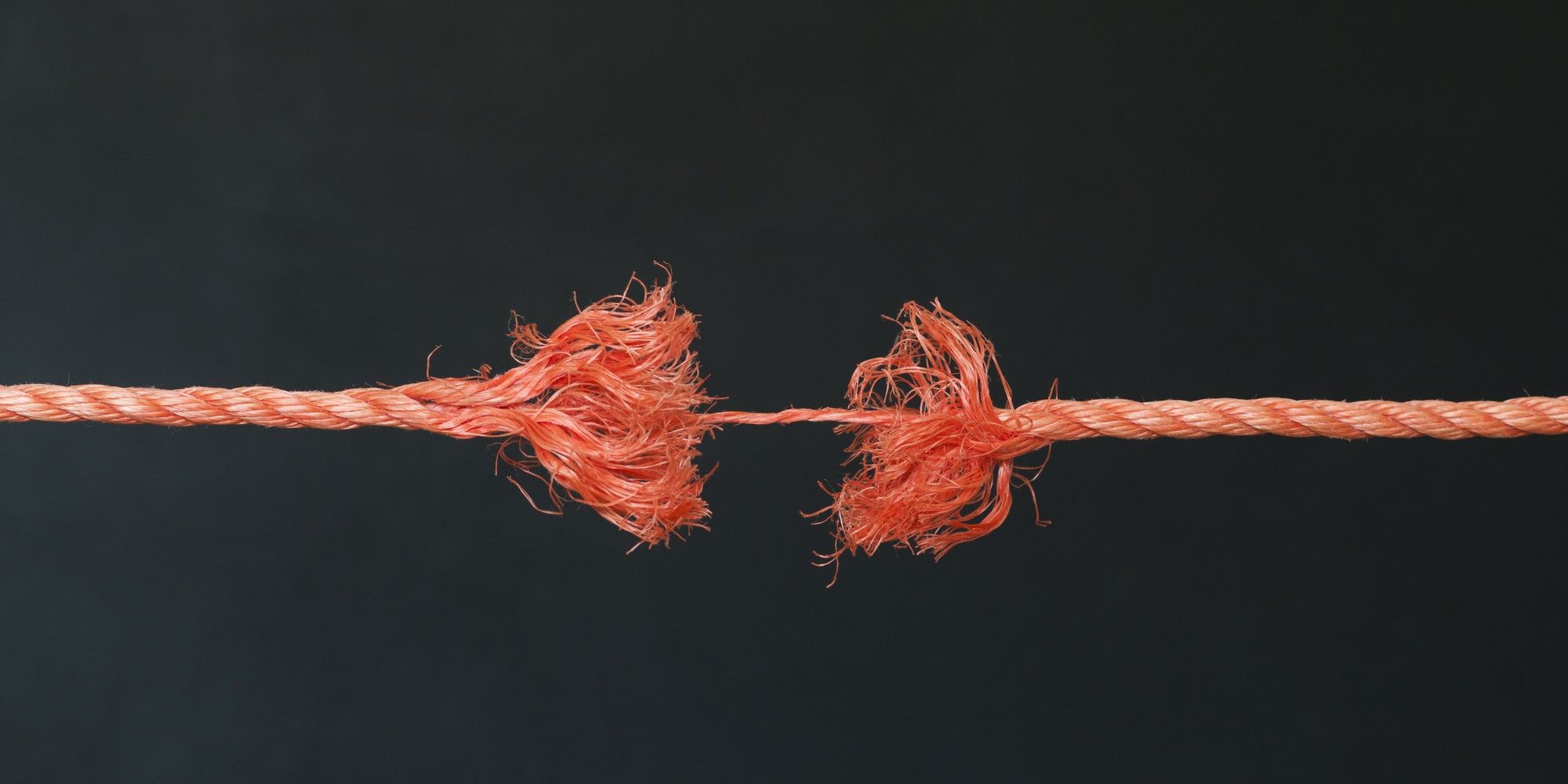 An orange rope frayed almost through, its two ends held together by a few thin strands against a dark background, standing for a customer relationship close to breaking.