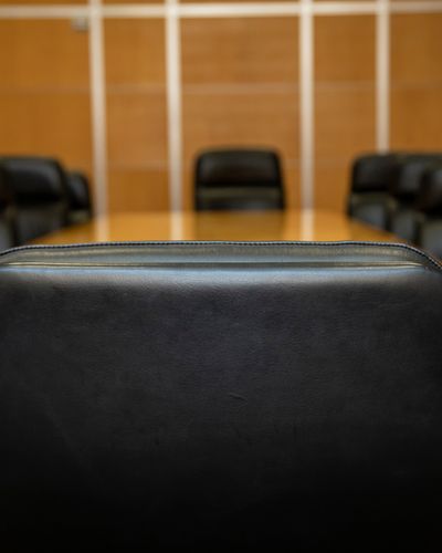 A clinical perspective view of an executive boardroom table, focusing on the vacant seat of authority to represent the structural redesign of the CMO role into a General Manager position.