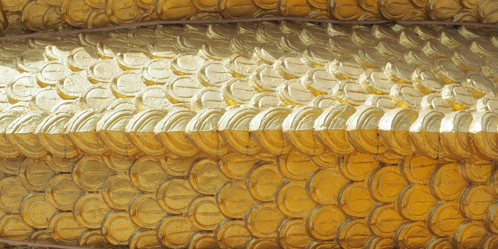 Rows of overlapping gold-painted scale-shaped relief tiles on a curved surface, evoking the layered costs hidden beneath a tempting free shipping offer.