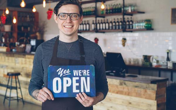 Small business owner standing in an Irish café holding an ‘Open’ sign — representing sales-based loans, merchant cash advance, and SME funding options in Ireland.