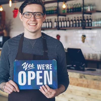Small business owner standing in an Irish café holding an ‘Open’ sign — representing sales-based loans, merchant cash advance, and SME funding options in Ireland.