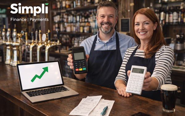 Two smiling pub owners stand behind a wooden bar holding different card payment devices, with a laptop, receipts, pen, pint of stout, and the white Simplí Finance | Payments logo visible in the top left, set against a warm traditional pub backdrop.