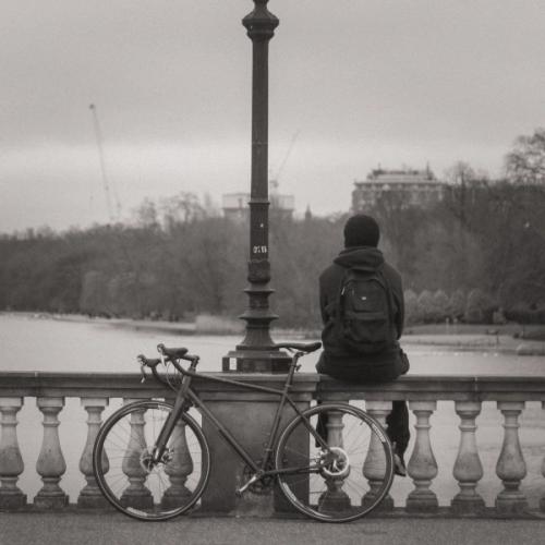 Person sitting on a bridge with the bike behind him