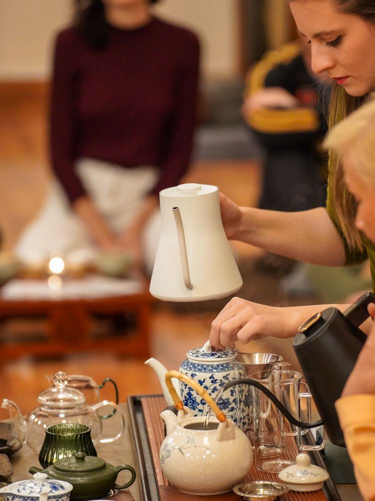 Teakiöntés fehér kannából, előtérben kék-fehér porcelán teáskannákkal.