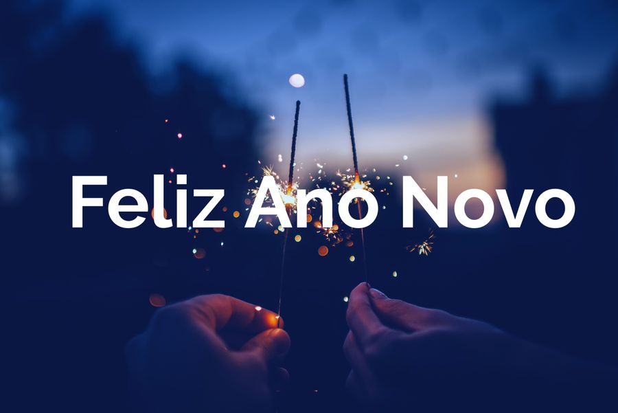 Mãos segurando estrelinhas de fogos de artifício acesas em céu noturno azul, com o texto Feliz Ano Novo em sobreposição