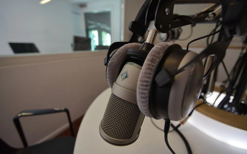 Microfone de estúdio em primeiro plano com fones de ouvido ao fundo, remetendo a uma cabine de narração esportiva