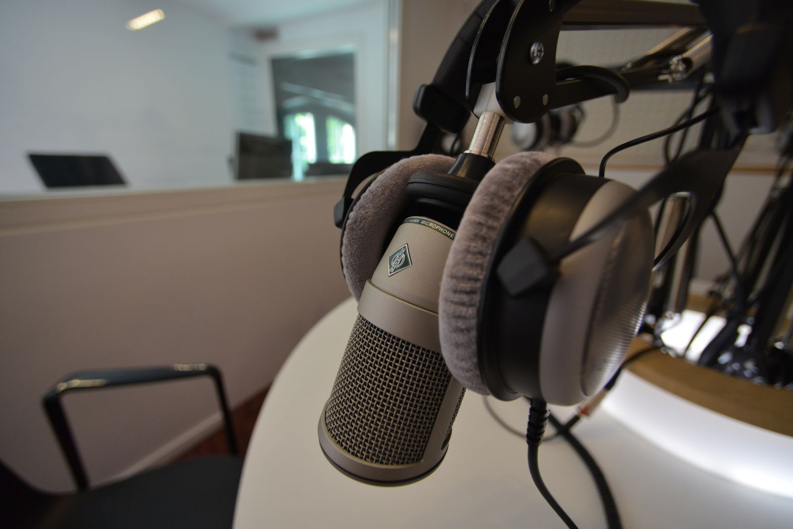 Microfone de estúdio em primeiro plano com fones de ouvido ao fundo, remetendo a uma cabine de narração esportiva