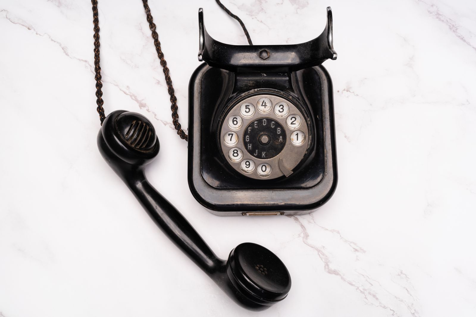 Telefone antigo preto com fone fora do gancho sobre superfície de mármore branco, remetendo à época em que se discava para saber a hora certa
