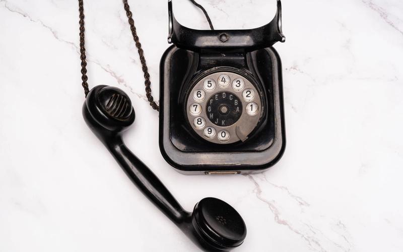 Telefone antigo preto com fone fora do gancho sobre superfície de mármore branco, remetendo à época em que se discava para saber a hora certa